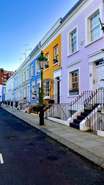 The image depicts a row of colorful Victorian-style terraced houses on a residential street, with facades painted in pastel shades of blue, yellow, and lavender. Each property has white-framed sash wi